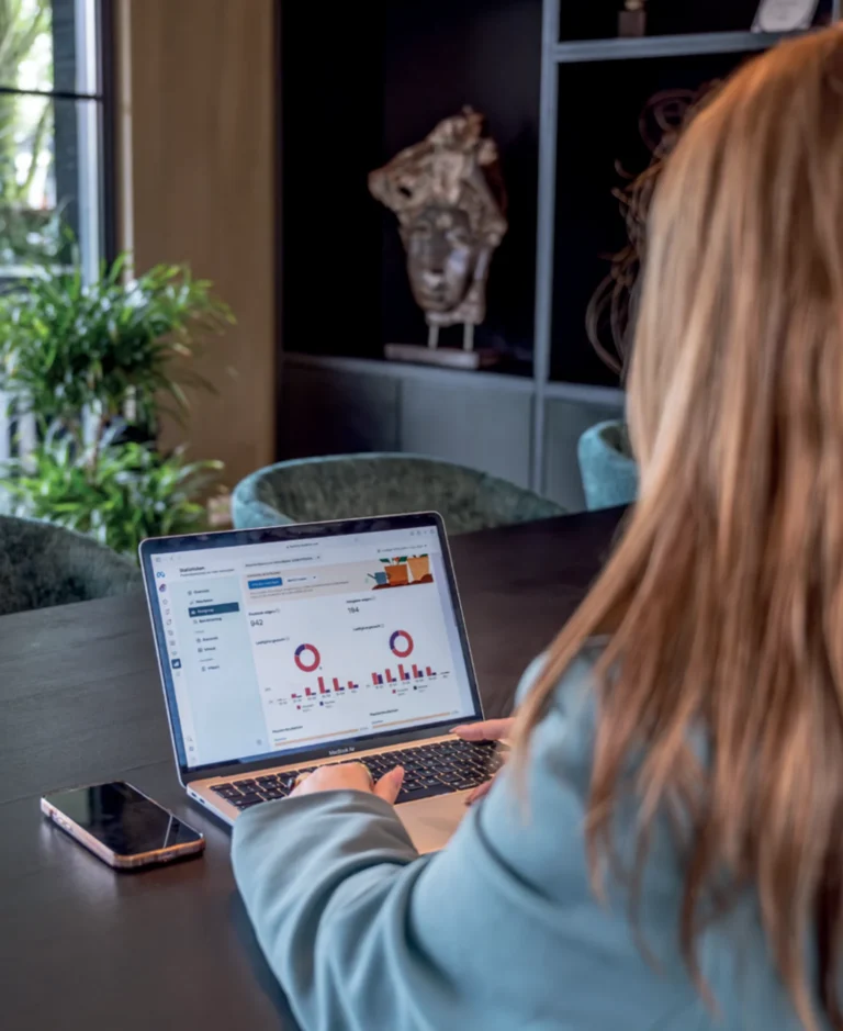 Person sitting at a dark table using a laptop to view business analytics dashboards with charts and graphs on screen