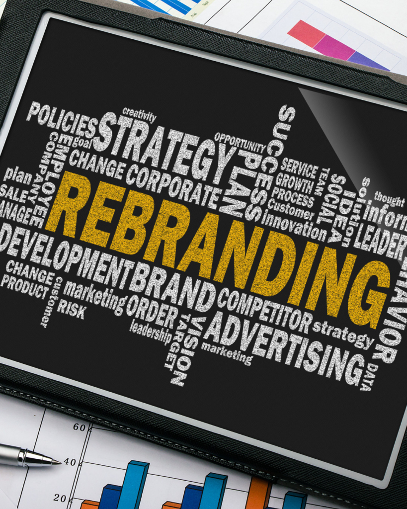 Tablet screen shows a yellow 'REBRANDING' word in a marketing word cloud, with related terms like strategy and advertising; charts and a pen in the background.