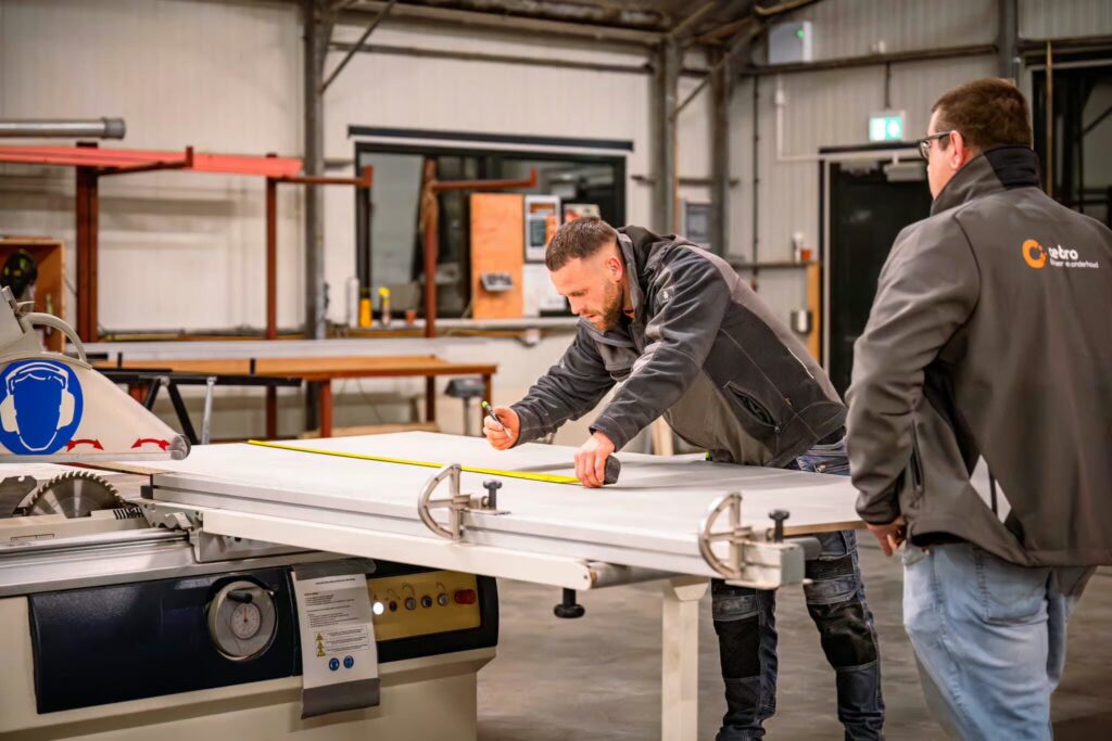Two men in a workshop measure a metal sheet on a large cutting machine.